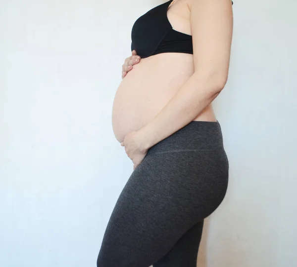 Una Mujer Embarazada Levanta Contra Una Pared Blanca Acaricia Vientre —  Fotos de Stock