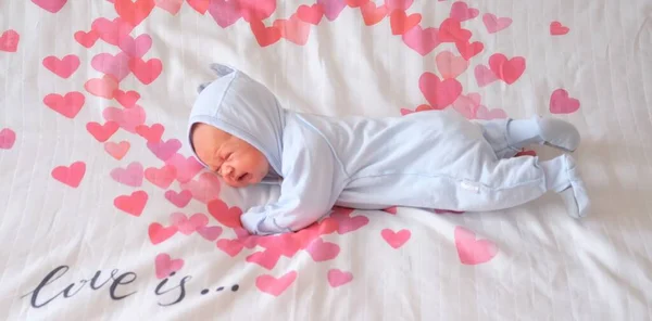 Un bebé recién nacido yace en la cama sobre una manta blanca con corazones rojos. — Foto de Stock