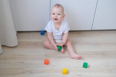 Küçük bir çocuk renkli küplerle yerde oynar ve onlardan bir piramit inşa eder..