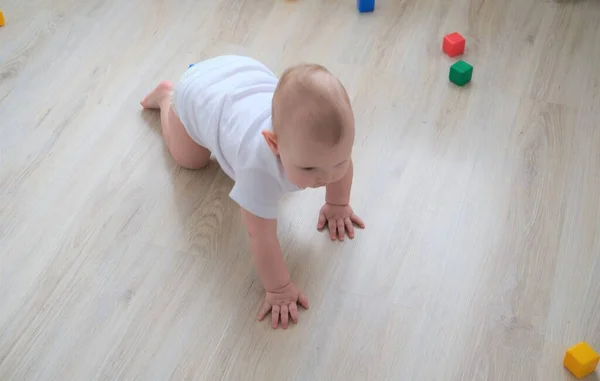 A small child plays on the floor with colored cubes and builds a pyramid out of them. — Stock Photo, Image