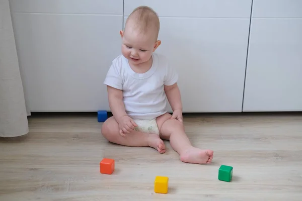 A small child plays on the floor with colored cubes and builds a pyramid out of them. — Stock Photo, Image