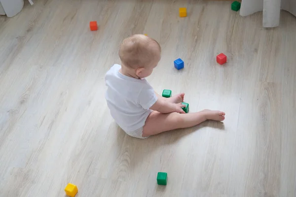 Een klein kind speelt op de vloer met gekleurde blokjes en bouwt er een piramide van.. Stockafbeelding