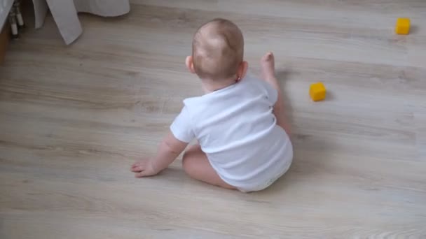 Uma criança pequena brinca no chão com cubos coloridos e constrói uma pirâmide deles. — Vídeo de Stock