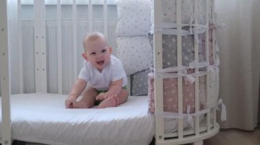 Çocuk beşiğinde oturur ve gülümser. Çocuk beşiğinde oynar.