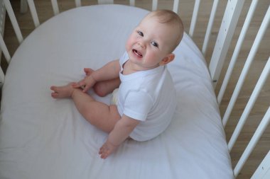 Çocuk beşiğinde oturur ve gülümser. Çocuk yatakta oynar.. 