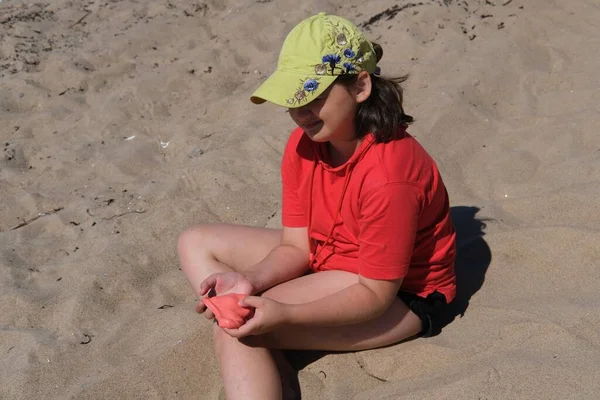 Das Mädchen hat roten Schleim in den Händen. Das Mädchen ist immer begeistert, mit Schleim zu spielen, selbst am Strand beruhigt das Spiel mit Schleim sie. — Stockfoto