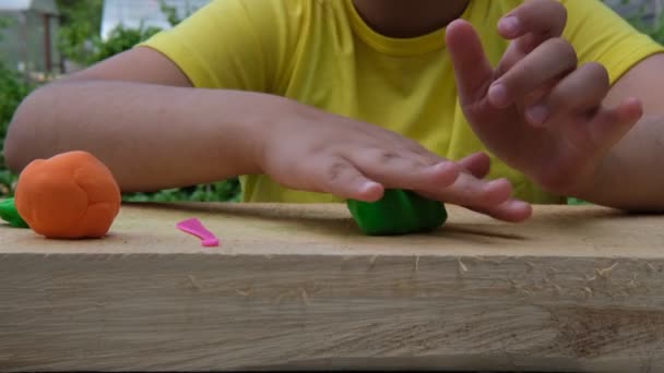 Ребенок делает различные фигуры на деревянной доске из мягкого разноцветного пластилина. Крупный план — стоковое видео