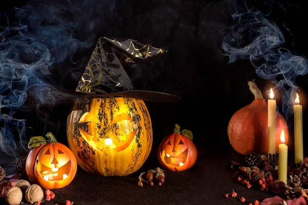 Carved Pumpkins for Halloween, Jack\'s head is on the table. Pumpkin in a witch\'s hat. Smoking a lighted candle. Dark background.