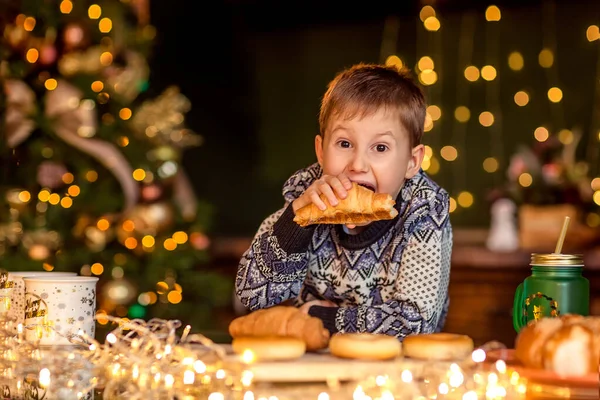 Boy Sits Table Decorated Christmas Kitchen Looks Croissant Wants Eat — Stock Photo, Image