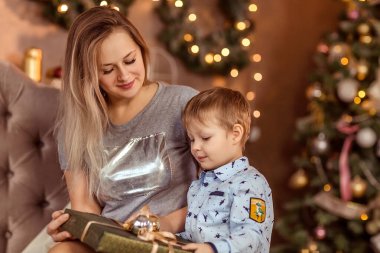 Gülümseyen genç kız ve oğlan süslü bir Noel odasında oturur ve bayramın ve hediyelerin tadını çıkarırlar. Seçici yumuşak odaklanma. Yana. Kış tatili konsepti.