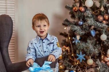4-5 yaşlarında güzel bir çocuk kanepenin yanında duruyor ve elinde hediyeler tutuyor. Kış tatili kavramı. Seçici yumuşak odak, bokeh (bulanık arkaplan).