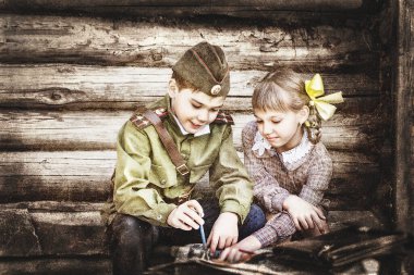 Zafer Günü için klasik olarak stilize edilmiş kartpostal. Askeri üniformalı bir çocuk ve eski elbiseli bir kız. 9 Mayıs, Rusya 'da Zafer Günü teması. Yumuşak seçici odak, eklenen gürültü.