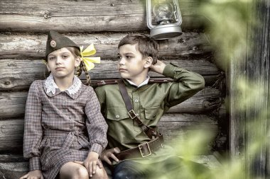 Zafer Günü için klasik olarak stilize edilmiş kartpostal. Askeri üniformalı bir çocuk ve eski elbiseli bir kız. 9 Mayıs, Rusya 'da Zafer Günü teması. Yumuşak seçici odak, eklenen gürültü.