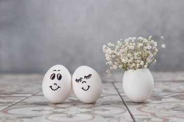 Paskalya kompozisyonu. Masada komik yüzlü beyaz yumurtalar. Yumurtadaki küçük bir buket. Paskalya 'nın asgari konsepti. Yazı için yeri olan bir Paskalya kartı..