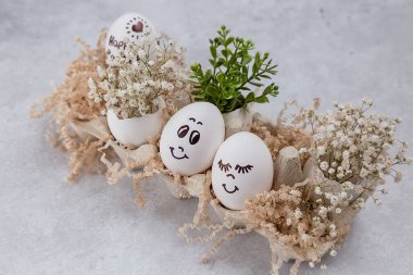 Paskalya kompozisyonu. Masada komik yüzlü beyaz yumurtalar. Yumurtadaki küçük bir buket. Paskalya 'nın asgari konsepti. Yazı için yeri olan bir Paskalya kartı..