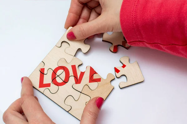 Girl connects (disconnects) wooden puzzles with the text Love. The concept of building or breaking love relationships. Top view
