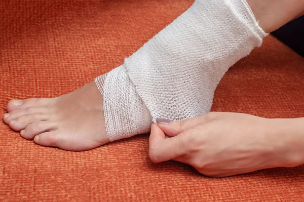 A young woman bandages her leg and lower leg with a bandage, pulls on an elastic bandage