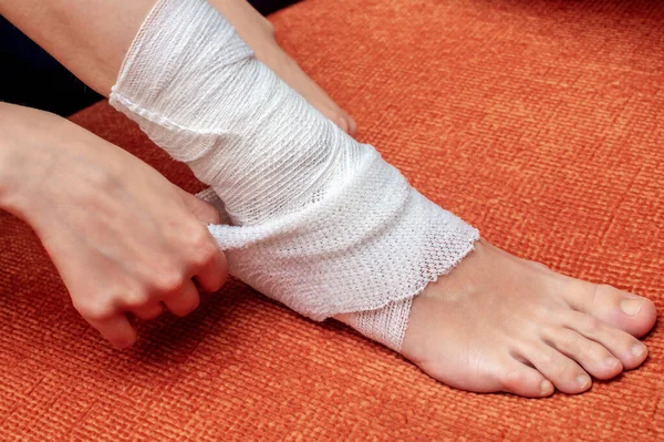 Young woman bandages her leg and lower leg with a bandage, pulls an elastic bandage over a gauze wrapped bandage for a secure fit.