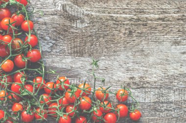 Ripe fresh cherry tomatoes with green branches on a wooden table. Light tint, top view.