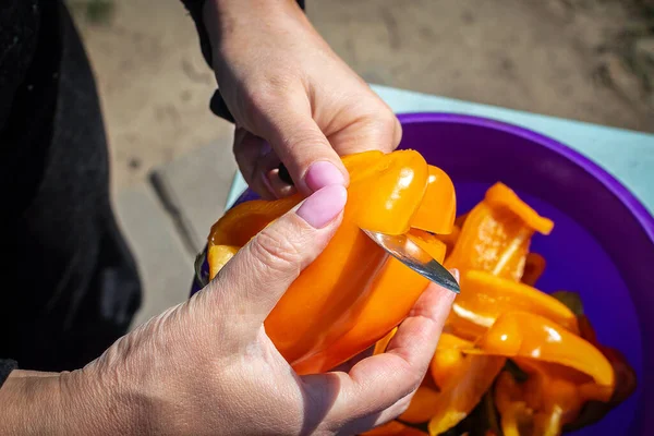 Womans tangan memotong paprika matang. Potongan lada jatuh ke dalam mangkuk salad plastik. Memasak salad lada matang segar selama piknik — Stok Foto