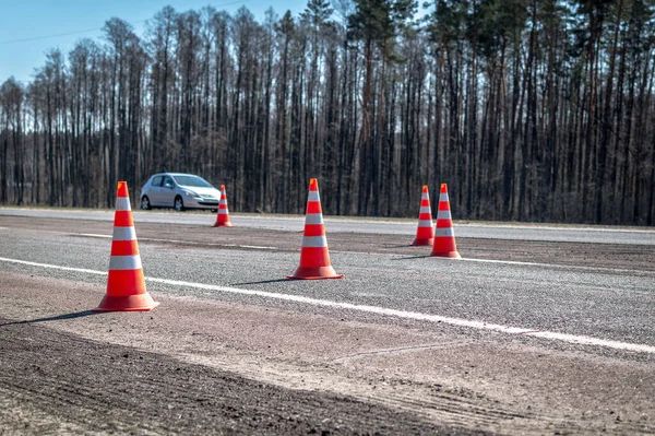 Road cones stands on the highway against the background of a fast-moving car. Safety cones or safety pylon on the asphalt. Road works, road repair in spring.