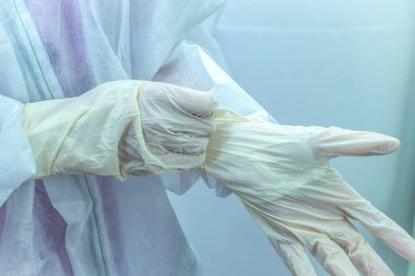 Koruyucu tıbbi antiviral giysi giyen tıp çalışanı tek kullanımlık beyaz eldivenler giyer..