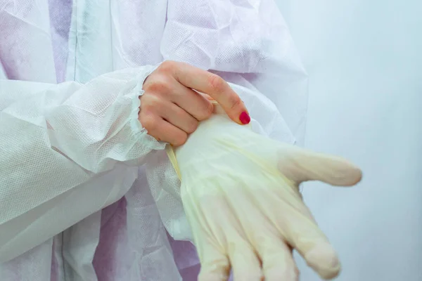 Young woman with painted nails putting on medical gloves and medical protective coverall. Close-up. Doctor in a protective suit to fight the epidemic of the disease.
