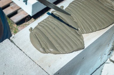 Havan topunu havalandırmalı beton EPS bloklardan bir duvar örmek için bir spatulayla döşemek. Özel bir evin dış duvarındaki ACC bloklarından kendi kendini inşa.
