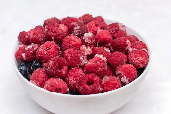 Frozen Summer Berries in a Bowl - Tasty Raspberries and blueberries. Bowl with frozen ripe berries on a white table — Stock Photo, Image