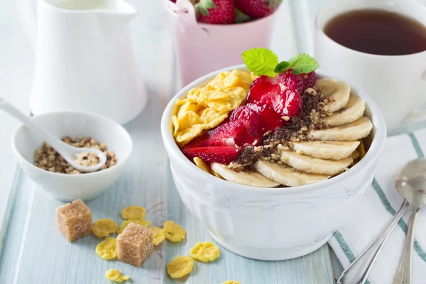Gesundes Frühstück. Cornflakes, Banane, Erdbeere, Mandel, Schokolade und Joghurt in einer Keramikschale auf hellem Hintergrund. — Stockfoto