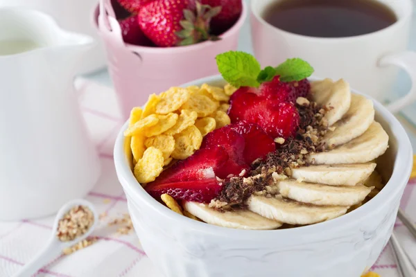 Hälsosam frukost. Corn flakes, banan, jordgubbar, mandel, choklad och yoghurt i en keramikskål på en ljus bakgrund. — Stockfoto