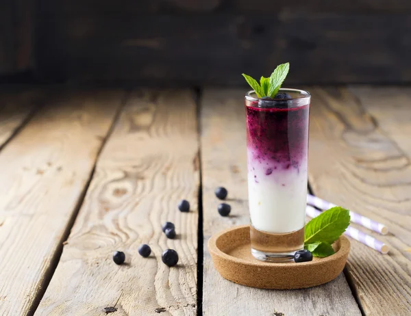 Smoothies de mirtilo saudável fresco em um copo com bagas e folhas de hortelã em um suporte de madeira.Foco seletivo . — Fotografia de Stock