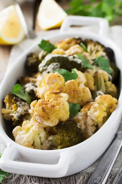 Coliflor al horno y brócoli con una salsa de tahini en un plato de cerámica blanca sobre fondo de madera vieja. Enfoque selectivo . —  Fotos de Stock