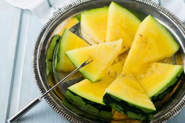 Hafif ahşap arka plan üzerinde demir tepsisindeki taze dilimlenmiş karpuz parçalar. Seçici odak.