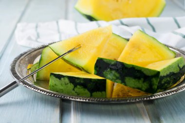 Hafif ahşap arka plan üzerinde demir tepsisindeki taze dilimlenmiş karpuz parçalar. Seçici odak.