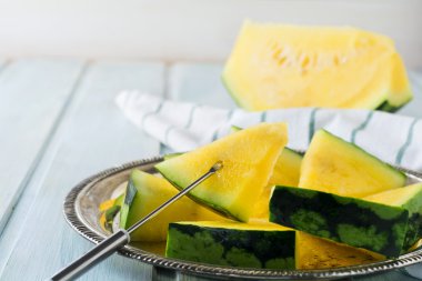 Hafif ahşap arka plan üzerinde demir tepsisindeki taze dilimlenmiş karpuz parçalar. Seçici odak.