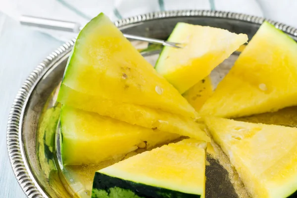 Hafif ahşap arka plan üzerinde demir tepsisindeki taze dilimlenmiş karpuz parçalar. Seçici odak.