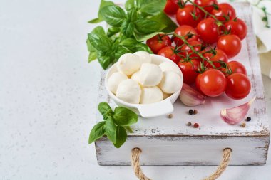 Mozzarella peynirli toplar, kiraz domatesleri ve yeşil taze organik fesleğen. İtalyan salata mutfağını hazırlamak için gerekli malzemeler.