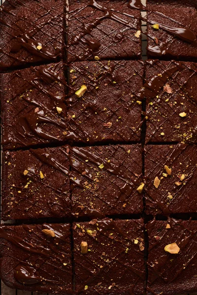 Quadrados de chocolate com pistache e morangos em um suporte de metal em um fundo de pedra leve, vista superior, composição horizontal. Depósito plano. — Fotografia de Stock