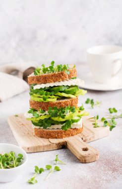 Avokado, salatalık ve beyaz peynirli sandviç. Sağlıklı bir kahvaltı için basit bir ahşap büfede mikro-yeşillik ve çok tahıllı ekmek ile süslenmiş. Seçici odak.