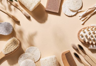 Sıfır atık banyo aksesuarı saç fırçası, bambu diş fırçası, çubuk, sünger taşı, lif bezi bej arka planda yeniden kullanılabilir alışveriş torbasında ahşap masaj bezi ve doğal sabun. Üst görünüm.