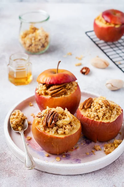 Four Red baked apples Stuffed with nut pecans, cinnamon, streyzel and honey on old concrete light background. Autumn or winter dessert. Selective focus.