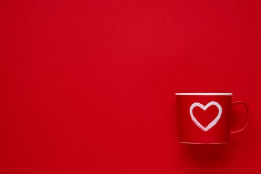 Kırmızı bardakta kırmızı ya da kırmızı arka planda kalbi boyanmış bir kupa. Düz kompozisyon. Sevgililer Günü konsepti. Üst görünüm, alanı kopyala.