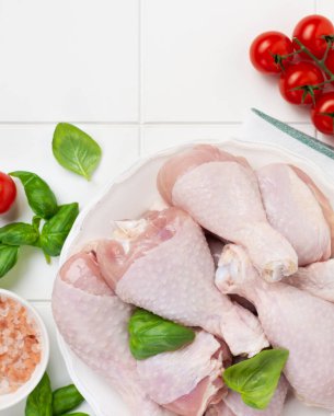 Çiğ tavuk eti, ızgara ya da barbekü için hazır, domatesli, otlu ve baharatlı açık beyaz mutfak masası arka planında. Üst görünüm.