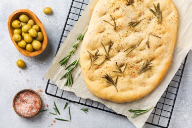 Taze pişirilmiş İtalyan geleneksel Focaccia ekmeği, baharatlar ve parşömen kağıdında biberiye ve açık gri arka plan. Üst görünüm