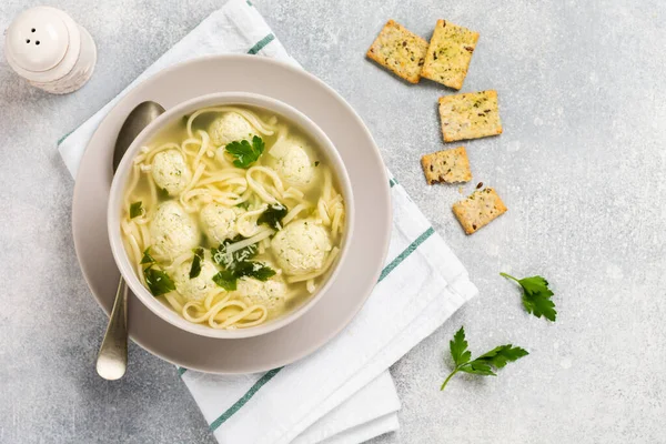 Ciotola di zuppa tradizionale italiana con polpette di pollo e pasta d'uovo, parmigiano, prezzemolo su sfondo grigio. Cucina tradizionale italiana. Vista dall'alto — Foto Stock