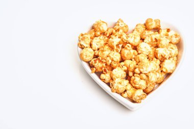 Beyaz arka planda izole edilmiş, beyaz seramik kalp tabağında karamel kaplı lezzetli patlamış mısır..