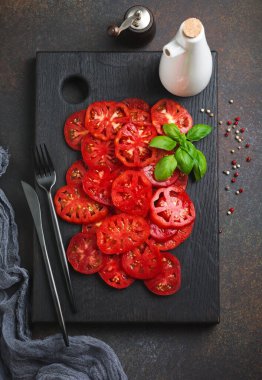 İtalyan caprese salatası için taze domates dilimleri biber, tuz ve fesleğen filizi ile siyah ahşap bir stantta zeytin yağı. Üst görünüm.