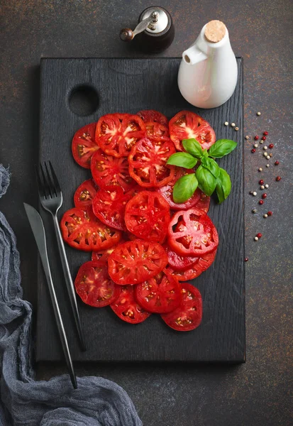 İtalyan caprese salatası için taze domates dilimleri biber, tuz ve fesleğen filizi ile siyah ahşap bir stantta zeytin yağı. Üst görünüm.