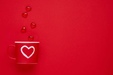Kırmızıda ya da kırmızı arka planda boyalı kalbi, şekeri ve çikolatası olan kırmızı bardak. Düz kompozisyon. Sevgililer Günü konsepti. Üst görünüm, alanı kopyala.